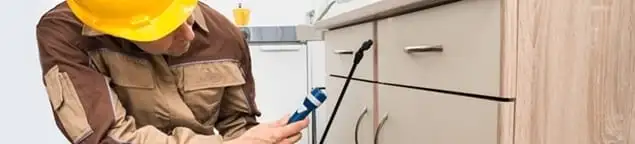 Roach exterminator applying treatment under kitchen cabinets in Santa Ana, CA