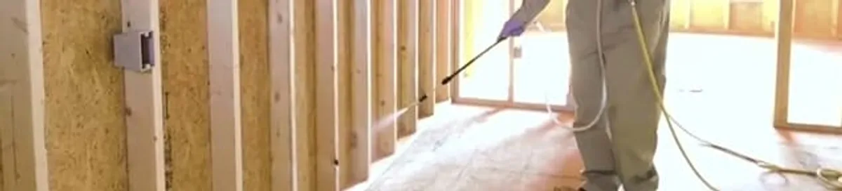 Termite treatment technician applying spray along framing and unfinished walls in Santa Ana, CA