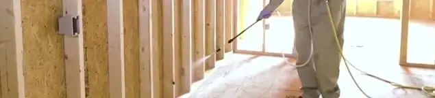 Termite treatment technician applying spray along framing and unfinished walls in Santa Ana, CA